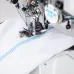 Close-up of the needle area on the Jack K5E industrial sewing machine, showing a tight, blue overlock stitch on white fabric.