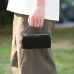 A person's hand holding the black BWOO BO-BS91 portable speaker by its woven carry handle outdoors.
