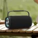 Black BWOO BO-BS91 portable speaker sitting on a wooden picnic table outdoors in bright light.