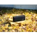 Black Sony portable Bluetooth speaker resting on a folded yellow blanket outdoors, surrounded by fallen yellow and orange autumn leaves.
