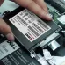 A hand is inserting the black XOC Nitro 256 GB solid state drive into a laptop's drive bay near a Dell battery.